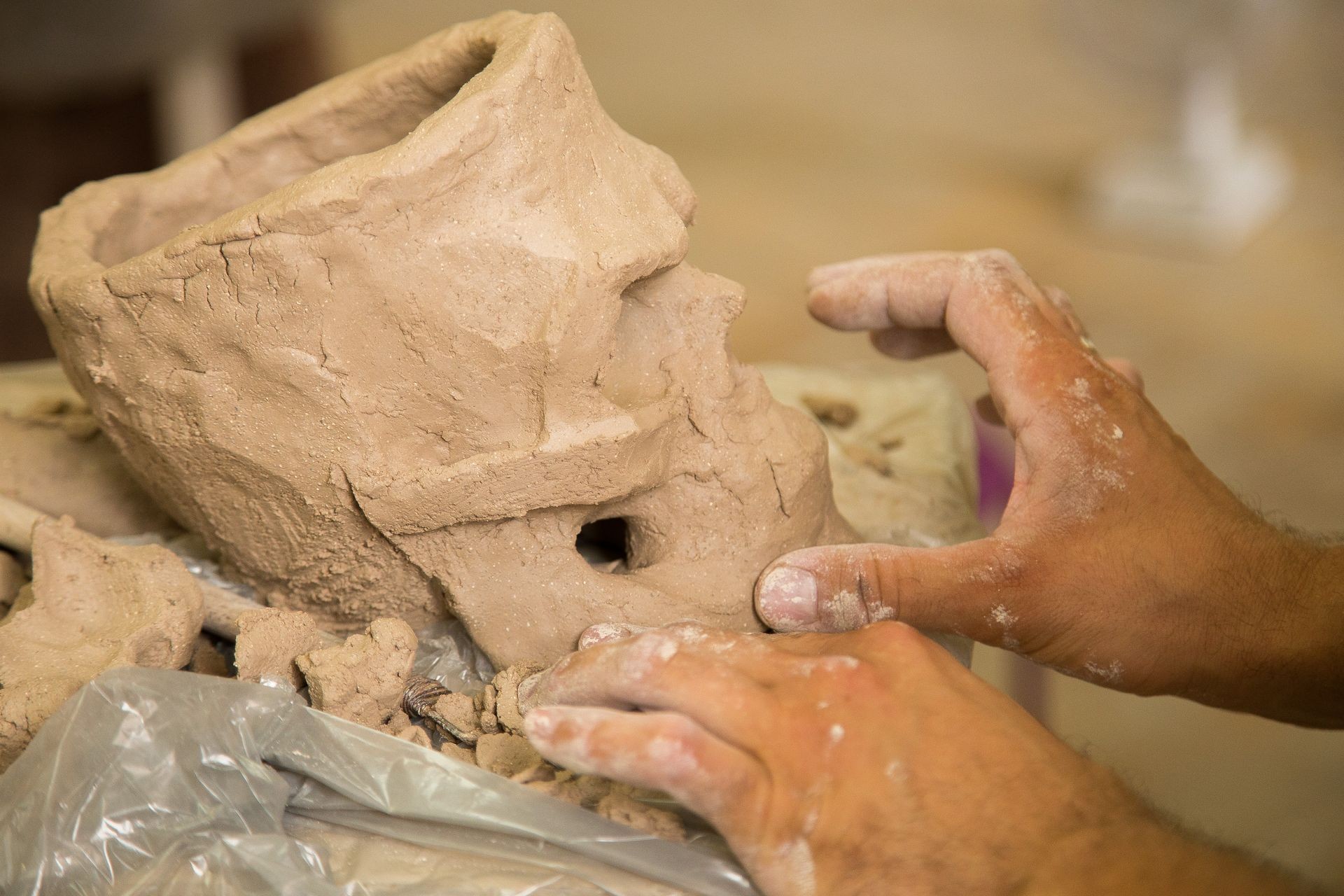 Sculptor modeling a skull out of raw clay with hands in a sculpting studio workshop